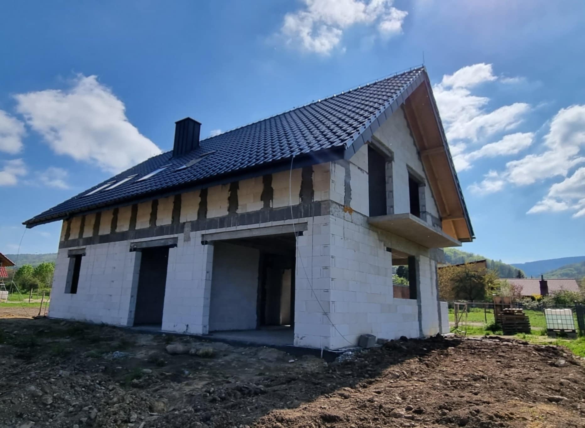 Dom w stanie surowym otwartym z ciemną dachówką, budowany w Dzierżoniowie, widok na góry w tle.