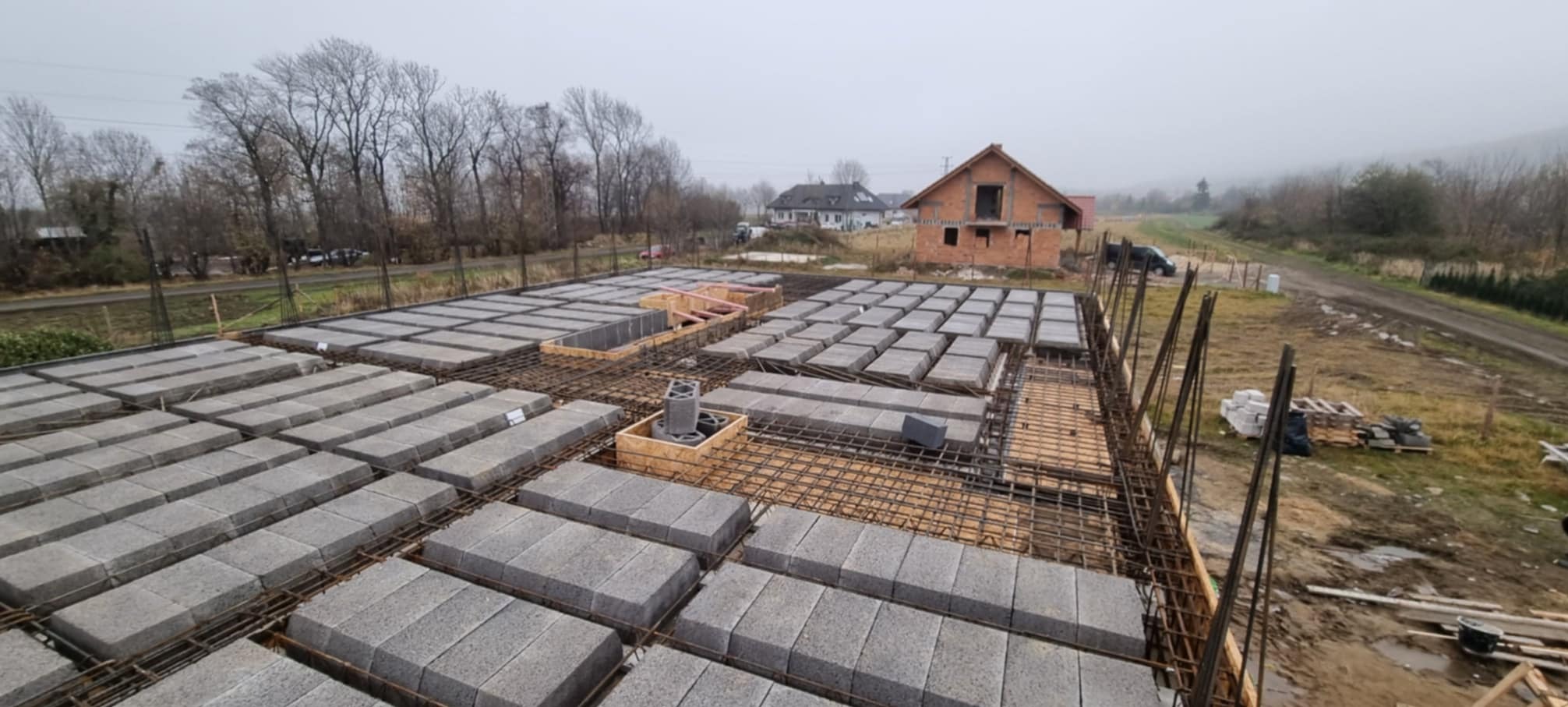 Przygotowanie zbrojenia i szalunku pod płytę fundamentową z pustaków szalunkowych na budowie domu jednorodzinnego w pochmurny dzień.