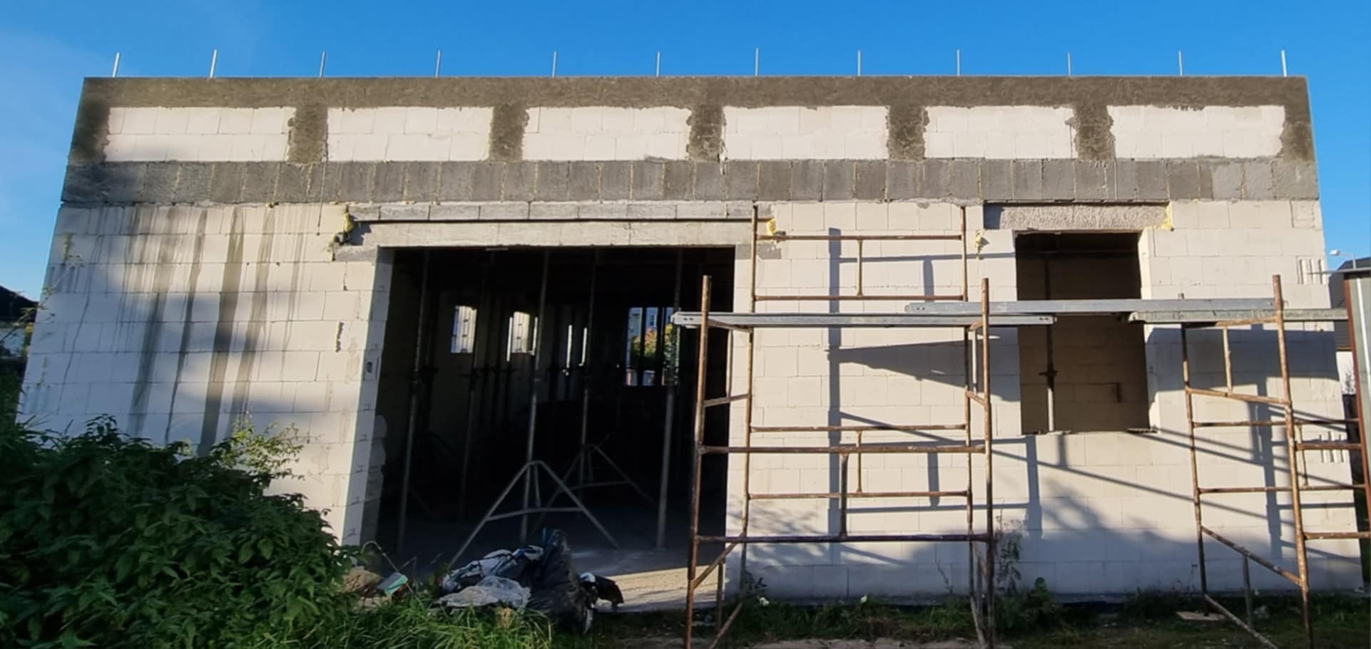 Budynek w trakcie wznoszenia ścian z betonu komórkowego, widoczne rusztowania i podpory stropu, częściowo wykonane nadproża okienne.