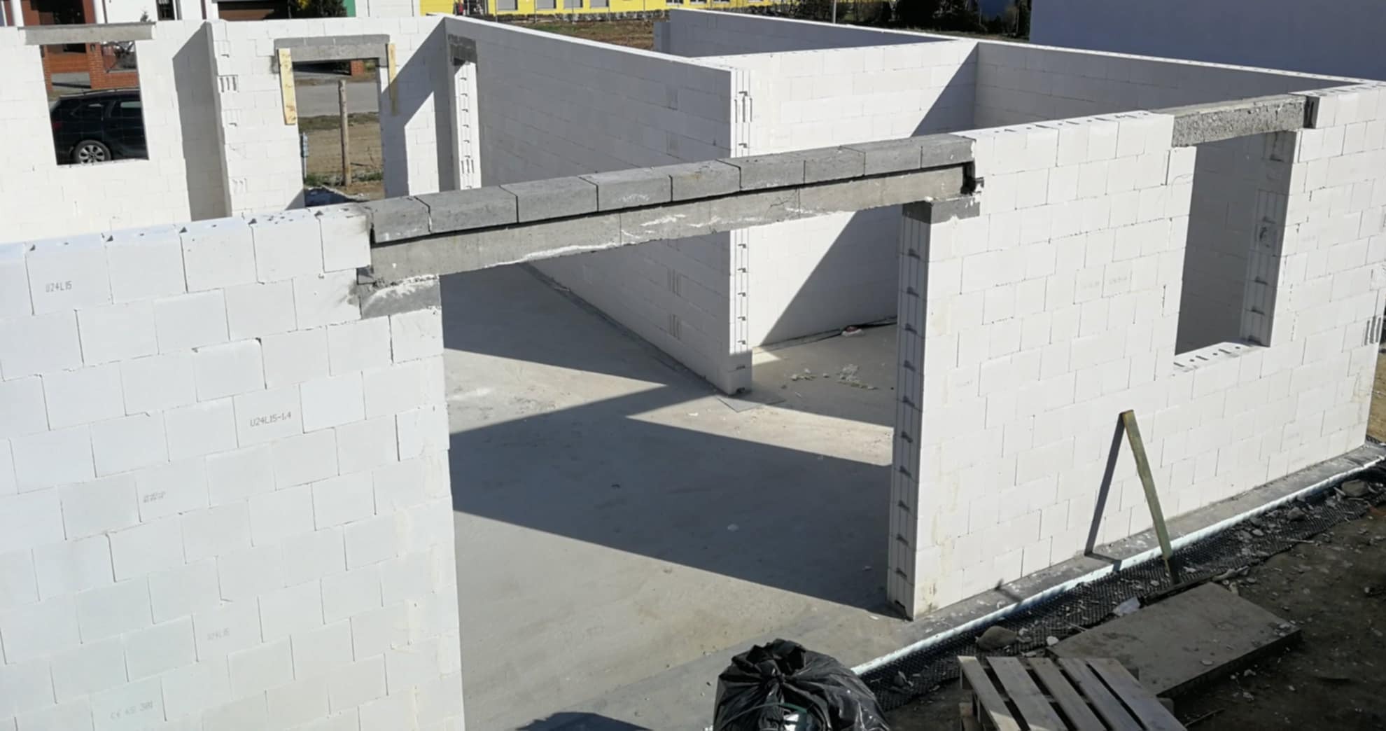 Surowy stan ścian domu w trakcie budowy, wykonane z białych bloczków z betonu komórkowego, z widocznymi nadprożami okiennymi i drzwiowymi oraz betonową wylewką podłogi.