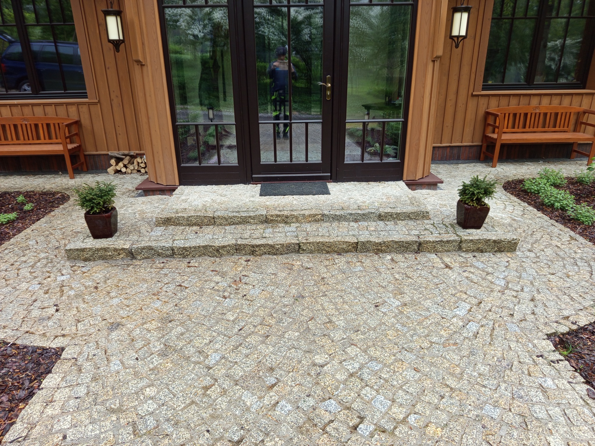 Ułożona kostka granitowa na podjeździe i schodach w Królówce. Widoczne dwie ławki i donice z roślinami. Eleganckie wykończenie posesji.