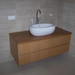 Nowoczesna szafka łazienkowa z umywalką nablatową w Kampinos. Drewniane fronty z subtelnymi uchwytami, jasne płytki w tle, minimalistyczna bateria.