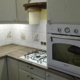 Jasna kuchnia z drewnianymi blatami i płytkami z motywami zwierzęcymi. Widoczny biały piekarnik i płyta gazowa. Uwagę zwracają ceramiczne uchwyty szuflad.