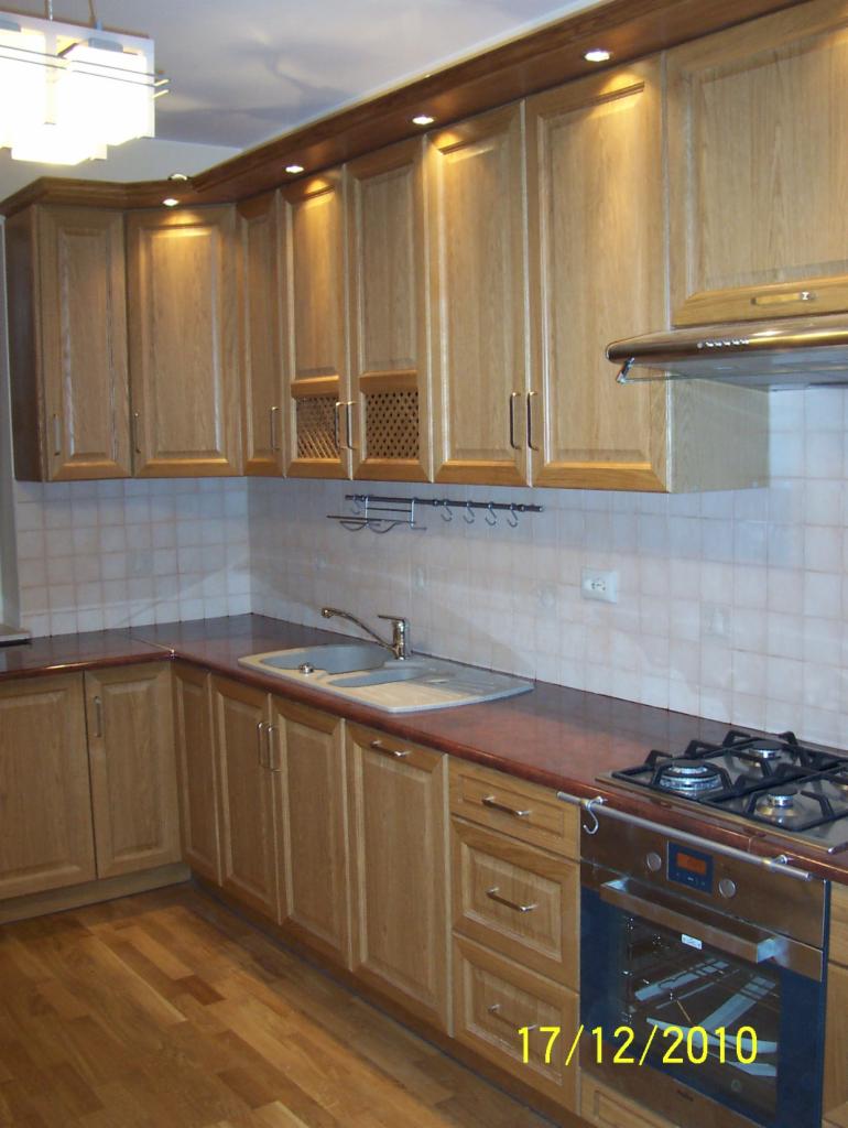 Jasna, drewniana zabudowa kuchenna z oświetleniem punktowym i kratkami wentylacyjnymi w górnych szafkach. Ustawna kuchnia z płytą gazową i piekarnikiem.