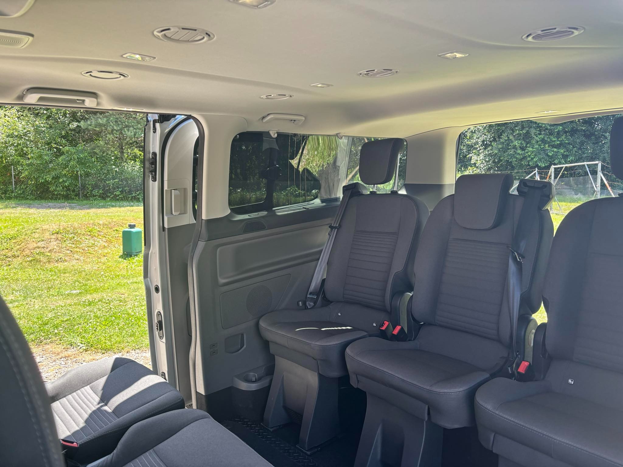 Wnętrze busa z widocznymi fotelami pasażerskimi, otwartymi drzwiami i zielonym krajobrazem za oknem.
