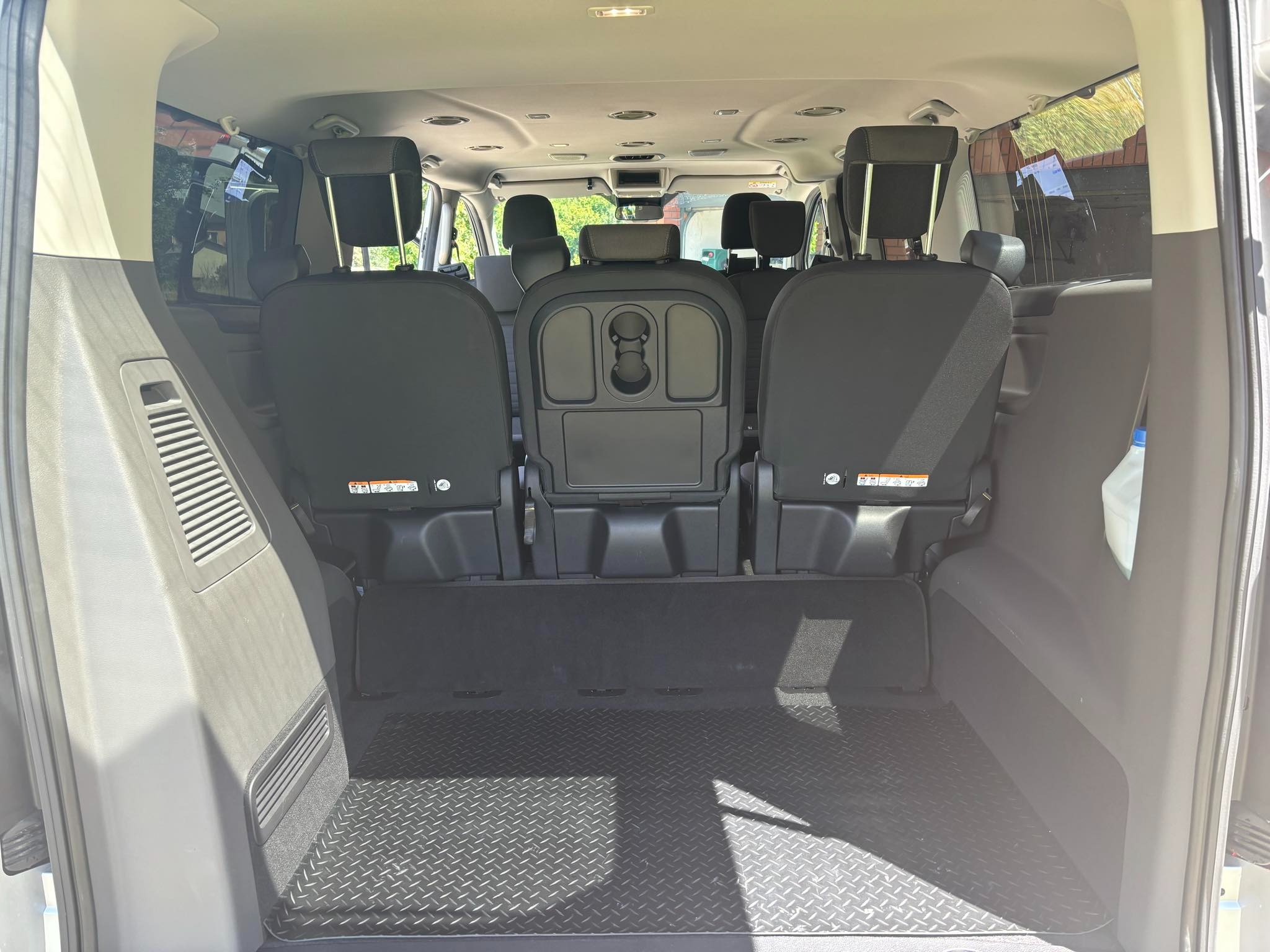 Wnętrze busa z trzema rzędami siedzeń, widok z tyłu na puste wnętrze bagażnika z gumową podłogą w romby.