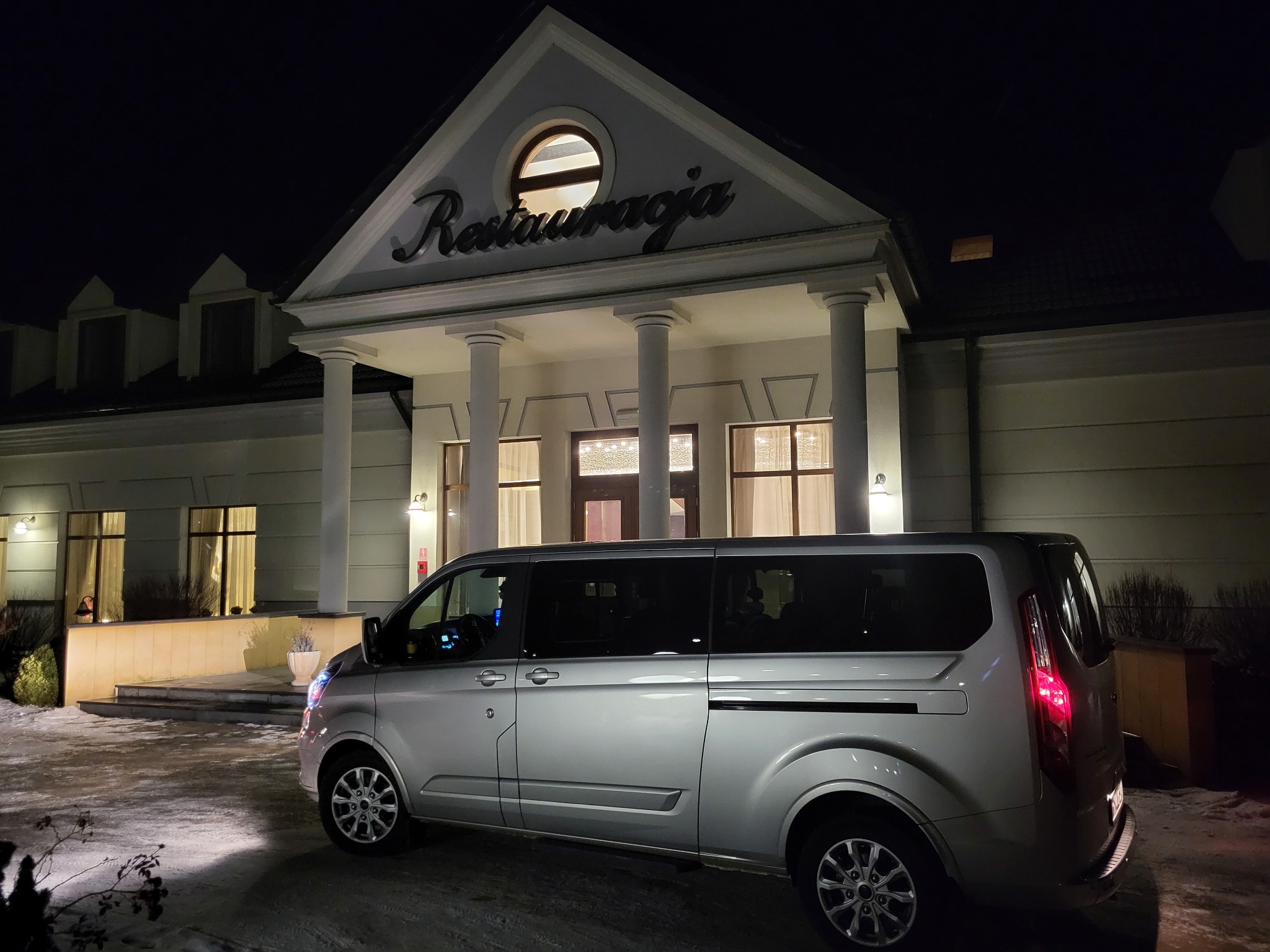 Srebrny van zaparkowany przed elegancką restauracją z kolumnami, nocne oświetlenie