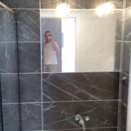 Kamil Furmanek - Ciemne, marmurkowe płytki w łazience z widocznym odbiciem osoby robiącej zdjęcie w lustrze, wiszące lampy sufitowe