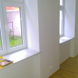 Kamil Furmanek - Białe, świeżo pomalowane ściany z dwoma oknami, marmurowe parapety, drewniana podłoga, widoczne ślady taśmy malarskiej na parapecie.