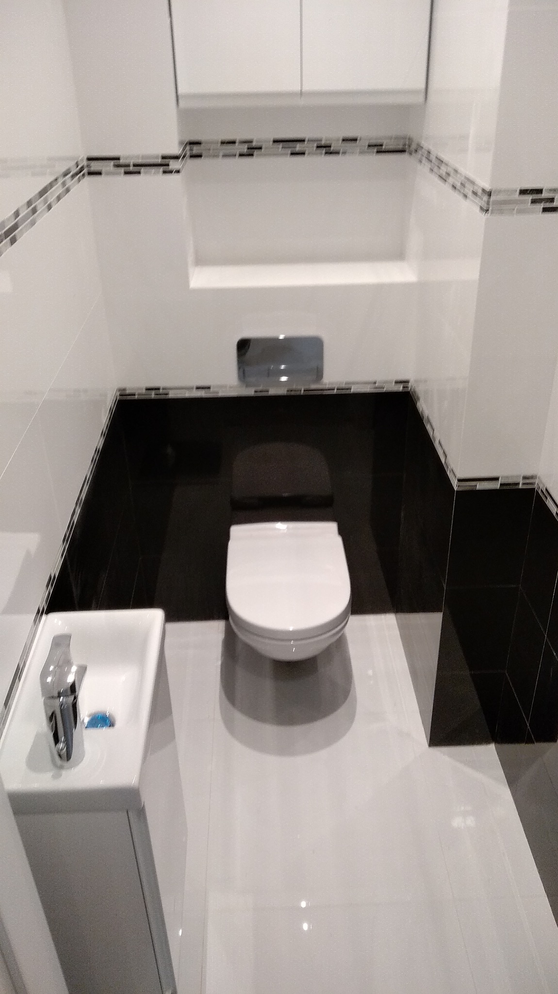 Wykończona łazienka w Łodzi z białą ceramiką, czarnymi płytkami na ścianach i podłodze, oraz dekoracyjnym paskiem mozaiki pod sufitem, prezentująca nowoczesny styl.