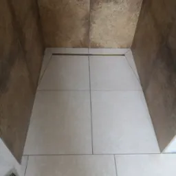 Wykończona kabina prysznicowa z beżowymi płytkami podłogowymi i brązowymi płytkami ściennymi, widoczny odpływ liniowy.