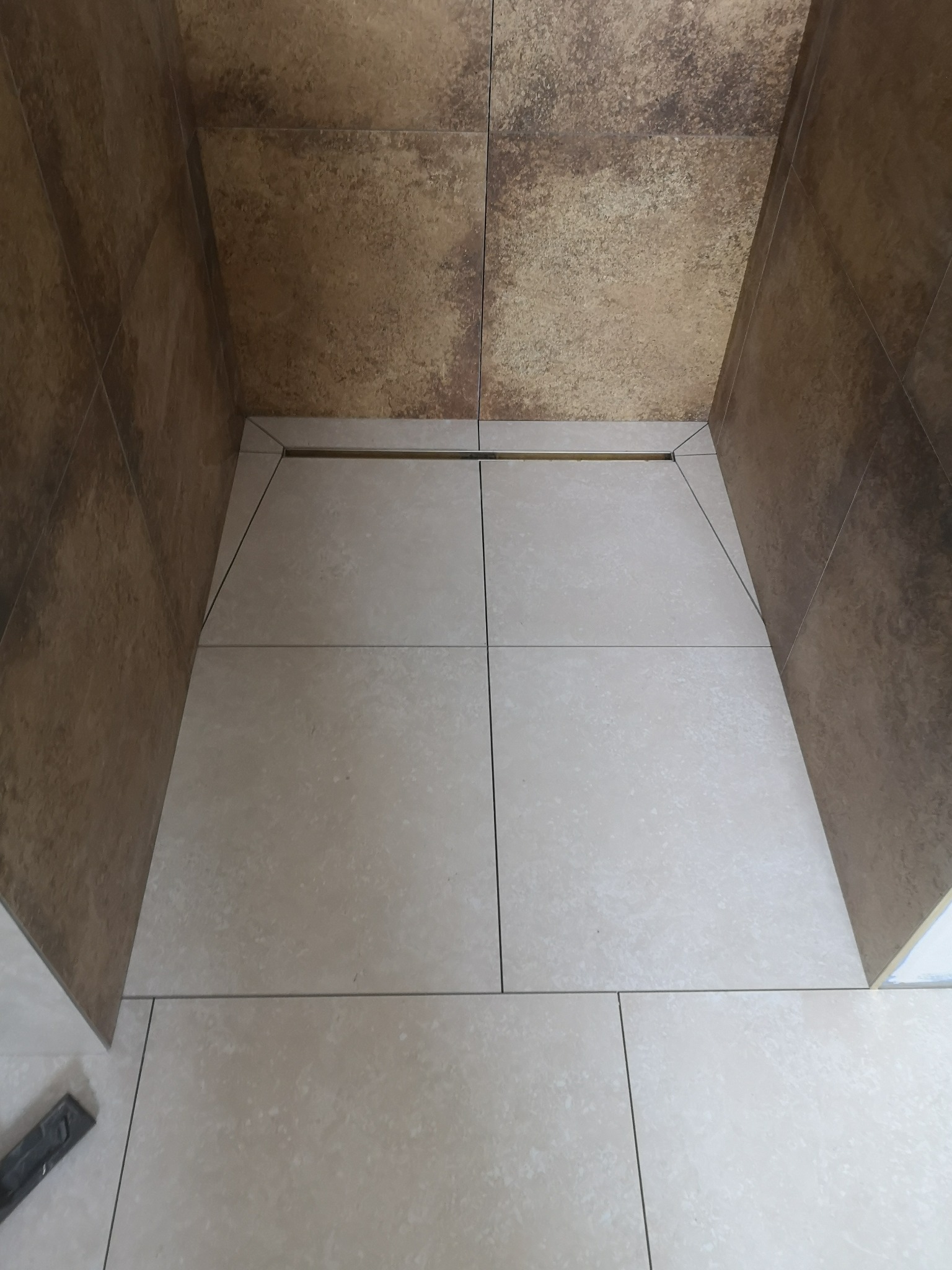 Wykończona kabina prysznicowa z beżowymi płytkami podłogowymi i brązowymi płytkami ściennymi, widoczny odpływ liniowy.