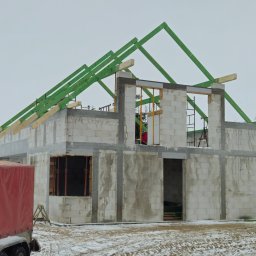 Firma Budowlana Jarosław Spiczak Brzeziński - Surowy stan domu z betonu komórkowego w Bytowie, z zielonymi elementami konstrukcji dachu i czerwonym przyczepą z plandeką w zimowej scenerii.