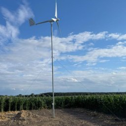 GLOBCORE - Niska turbina wiatrowa z trzema śmigłami, zainstalowana na polu kukurydzy, zabezpieczona linami odciągowymi, widok w słoneczny dzień pod błękitnym niebem.