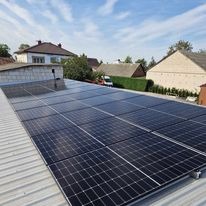 Rząd paneli słonecznych Jinko Solar 480 W na dachu budynku mieszkalnego, widok z góry, błękitne niebo z delikatnymi chmurami w tle.