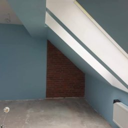 O&O Dominik Pawłowski - Pokój na poddaszu po świeżym pomalowaniu ścian na niebiesko, z widocznym wałkiem malarskim na podłodze i fragmentem ściany z cegły.