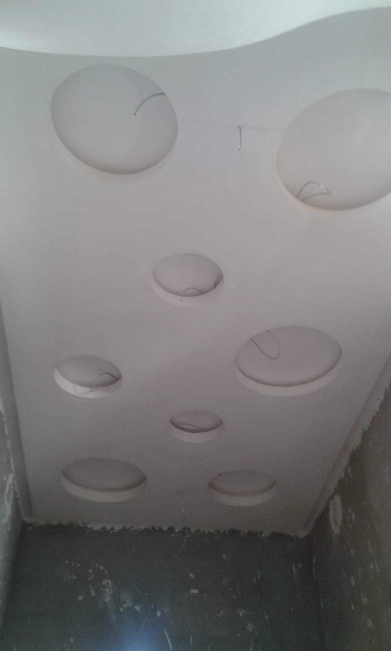 Biały sufit z okrągłymi wgłębieniami w kształcie okręgów, widoczne niedociągnięcia w wykończeniu, szpachla na ścianach.