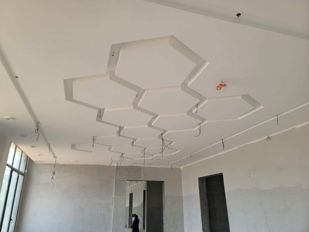Sufit z dekoracyjnymi elementami gipsowymi w kształcie heksagonów, w trakcie montażu instalacji elektrycznej, widoczne przewody, surowe ściany w tle.