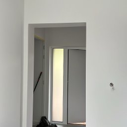 Maciej Siwiec - Białe ściany po malowaniu, zabezpieczone taśmą malarską przy suficie i gniazdkach. Widoczny odkurzacz przemysłowy i folia ochronna na podłodze.