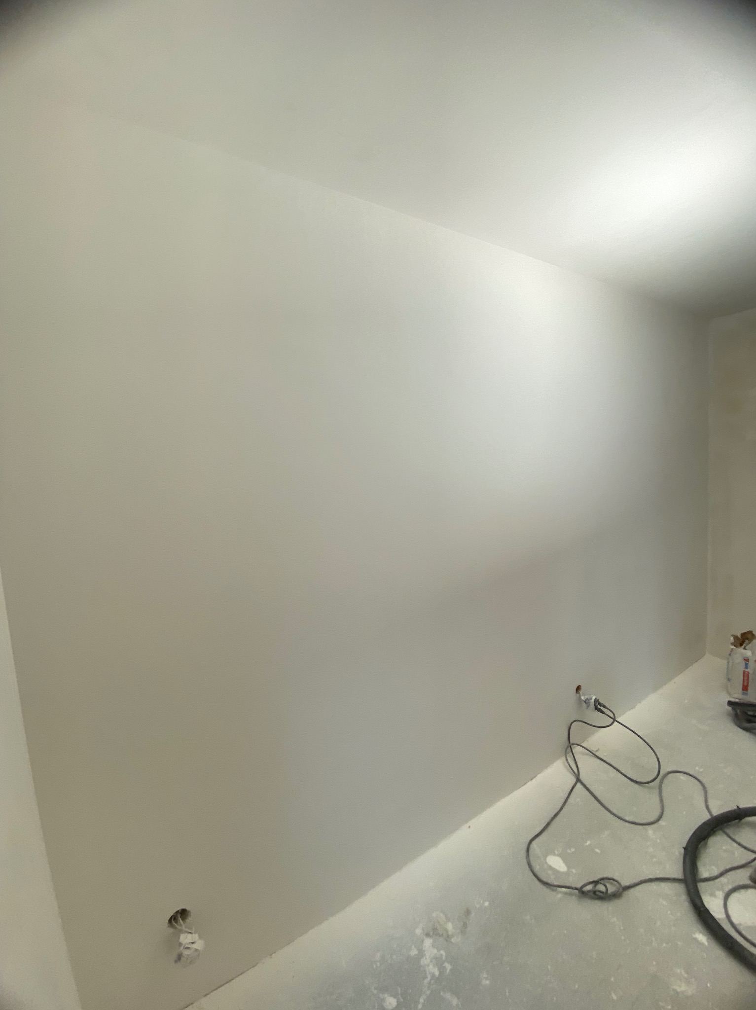 Gładka, biała ściana po szpachlowaniu, widoczny kabel i odkurzacz. Świeżo wykończone wnętrze, gotowe do dalszych prac wykończeniowych.