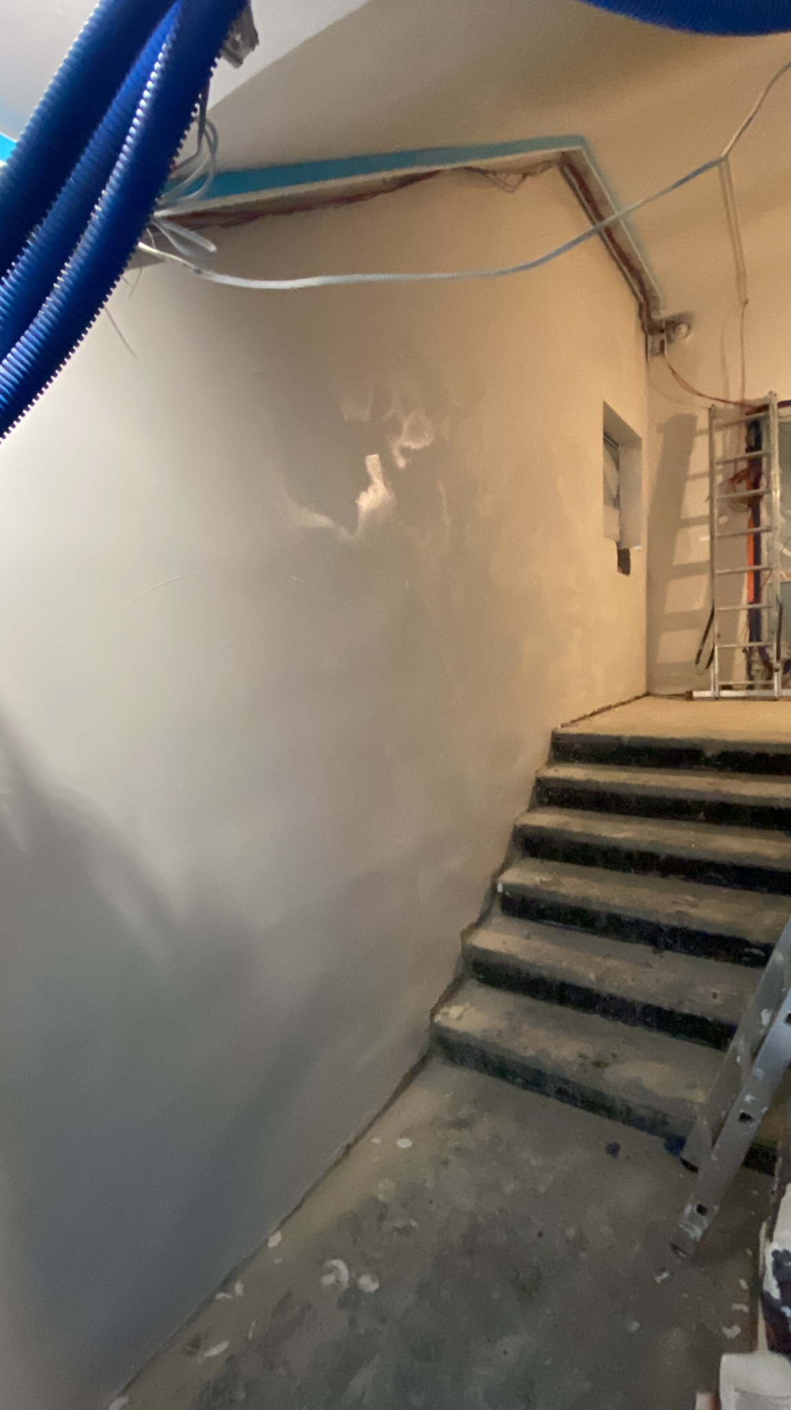 Ściana po szpachlowaniu, widoczne schody i drabina. Instalacje na suficie. Wykończenie wnętrza w trakcie prac, przygotowanie do malowania.