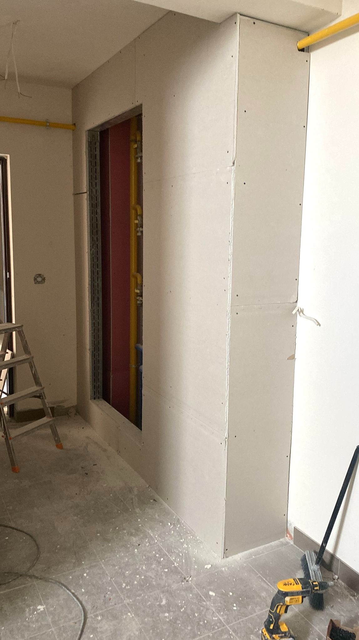 Montaż płyt karton-gips na ścianie z widoczną instalacją wewnątrz. Fragment pomieszczenia w trakcie remontu, widoczny drabina i narzędzia.