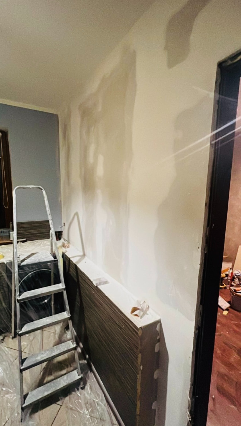 Ściana po szpachlowaniu, przygotowana do malowania. Widoczna drabina i płyty karton-gips. Podłoga zabezpieczona folią. Ujęcie z perspektywy podłogi.