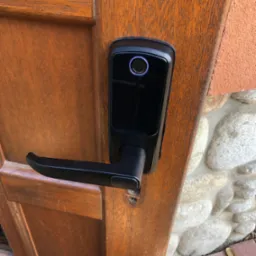 Drewniane drzwi z nowoczesnym, czarnym zamkiem elektronicznym z czytnikiem linii papilarnych. Widoczne narzędzia wskazują na montaż.