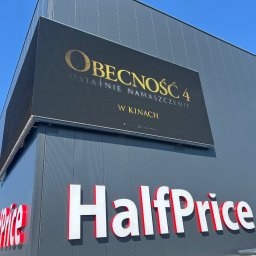 NKTelektrick - Elewacja budynku HalfPrice z LED ekranem wyświetlającym reklamę filmu 'Obecność 4'. Szary budynek, biało-czerwone logo. Błękitne niebo.