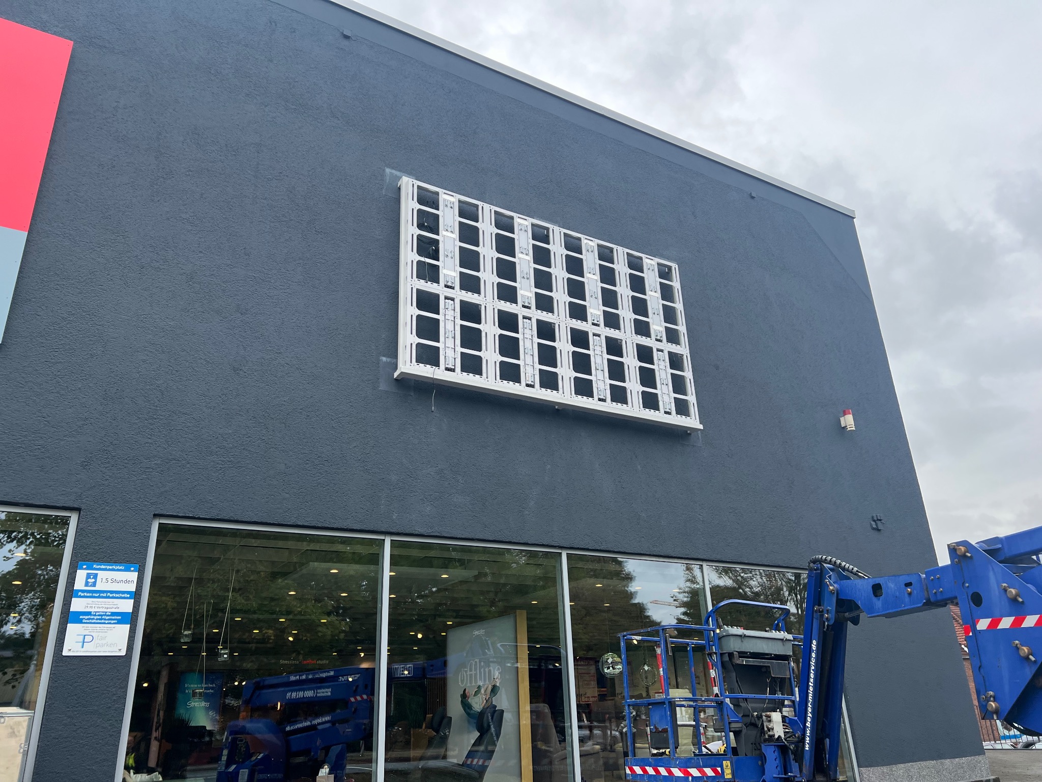 Montaż ramy pod ekran LED na szarej fasadzie budynku. Widoczny podnośnik koszowy i fragment witryny sklepowej.