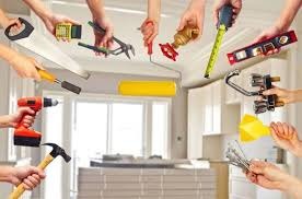 Różnorodne narzędzia budowlane i elektryczne trzymane w dłoniach na rozmytym tle wnętrza, w tym wiertarka, młotek, poziomica, piła, klucze, miernik, pędzel malarski i złączki elektryczne.