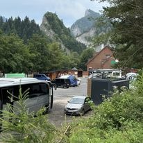 Parking z różnymi pojazdami transportowymi, w tle góry i zieleń, widok z lekkiej góry.