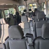 Wnętrze busa pasażerskiego z szarymi fotelami i zagłówkami, widok z tyłu pojazdu w kierunku przednich siedzeń.