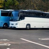 Dwa autokary na parkingu: błękitny i biały, z widocznym logo na białym pojeździe.