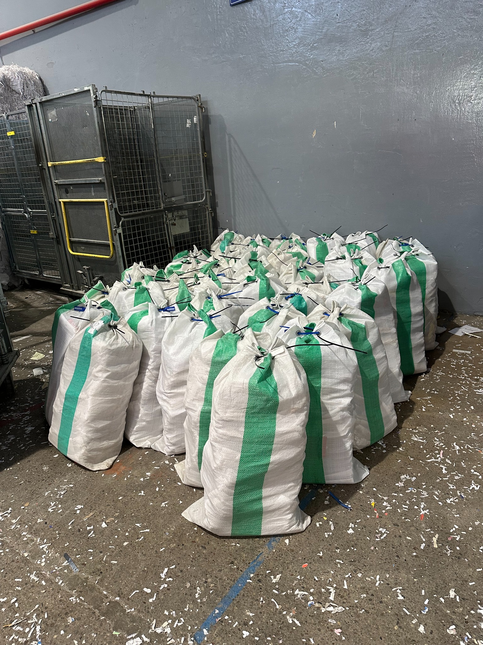 Wypełnione worki z pociętymi dokumentami, ustawione w magazynie w pobliżu metalowych wózków, na podłodze porozrzucane strzępy papieru.