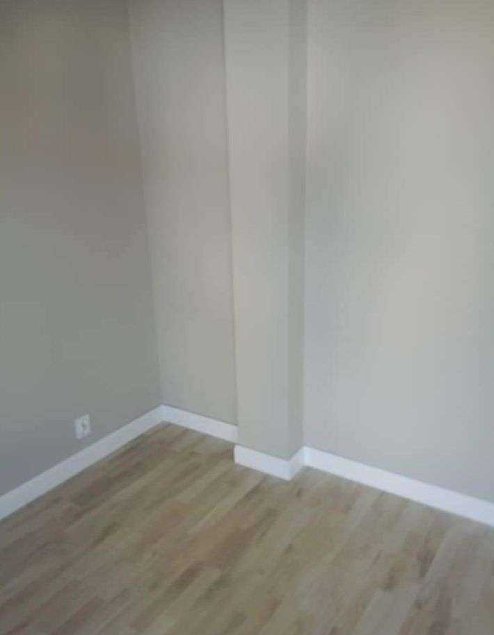 Wnętrze pokoju po remoncie: świeżo ułożony parkiet z jasnego drewna, pomalowane na beżowo ściany i białe listwy przypodłogowe.