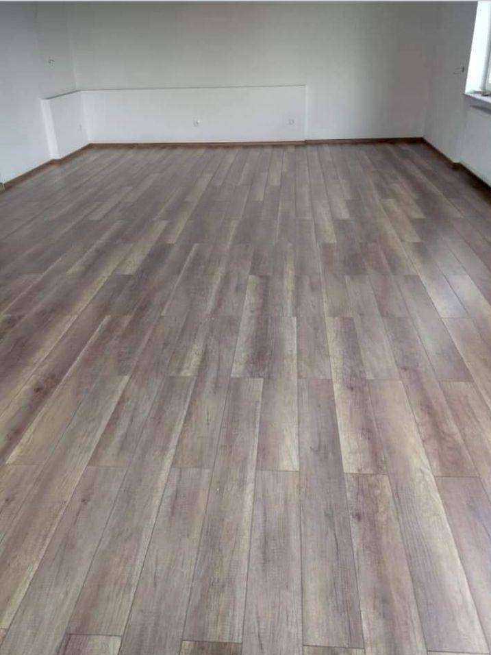 Ułożona podłoga z paneli imitujących drewno w pustym, jasnym pomieszczeniu z białymi ścianami i niskim oświetleniem.