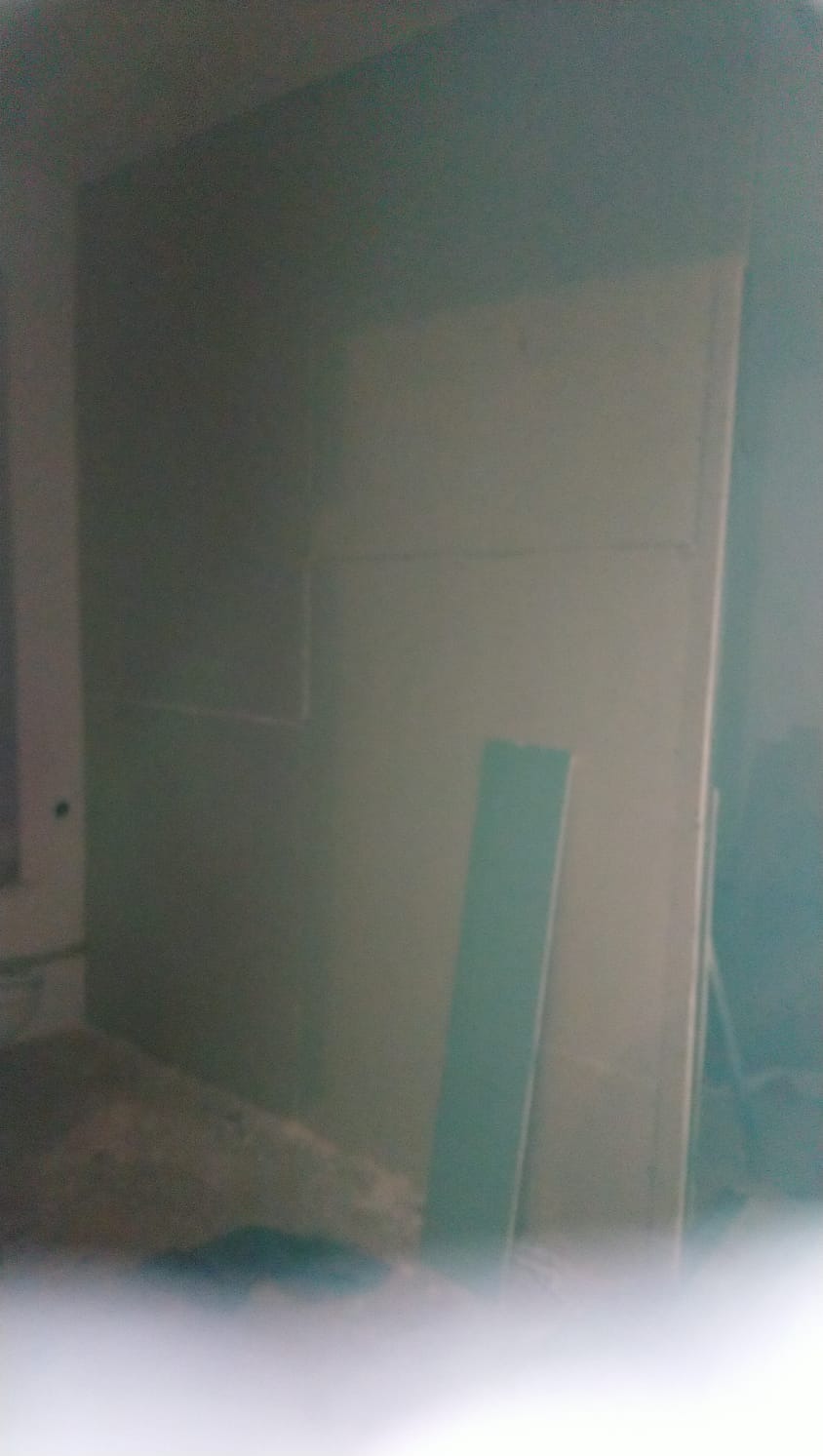 Świeżo pomalowana, gładka ściana w odcieniach szarości, z widocznymi śladami po taśmie malarskiej i niedoskonałościami w dolnej części, oświetlona z prawej strony, z fragmentem listwy...