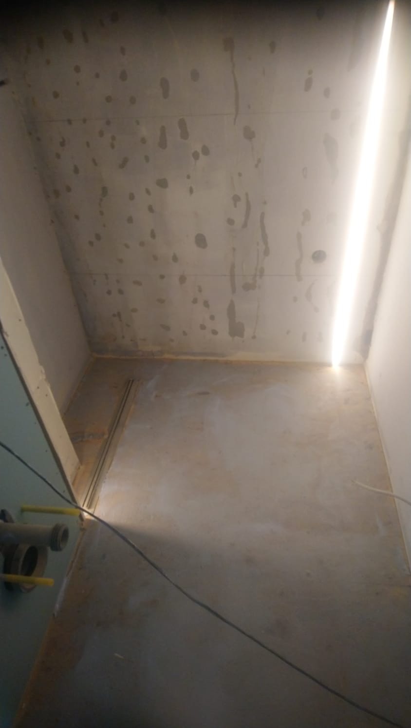 Surowy stan ścian i podłogi w łazience przed wykończeniem, widoczne ślady po zalaniu na suficie, instalacja kanalizacyjna przy ścianie.