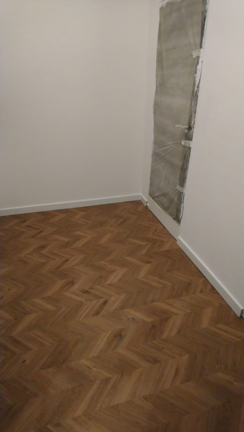 Pokój po remoncie z parkietem ułożonym w jodełkę; drzwi zabezpieczone folią malarską.