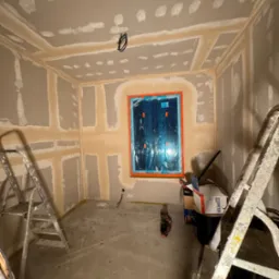 Pokój w trakcie prac przygotowawczych do wykończenia ścian, widoczne płyty kartonowo-gipsowe na ścianach i suficie, zaszpachlowane łączenia, okno zabezpieczone folią, drabiny w pomieszczeniu.