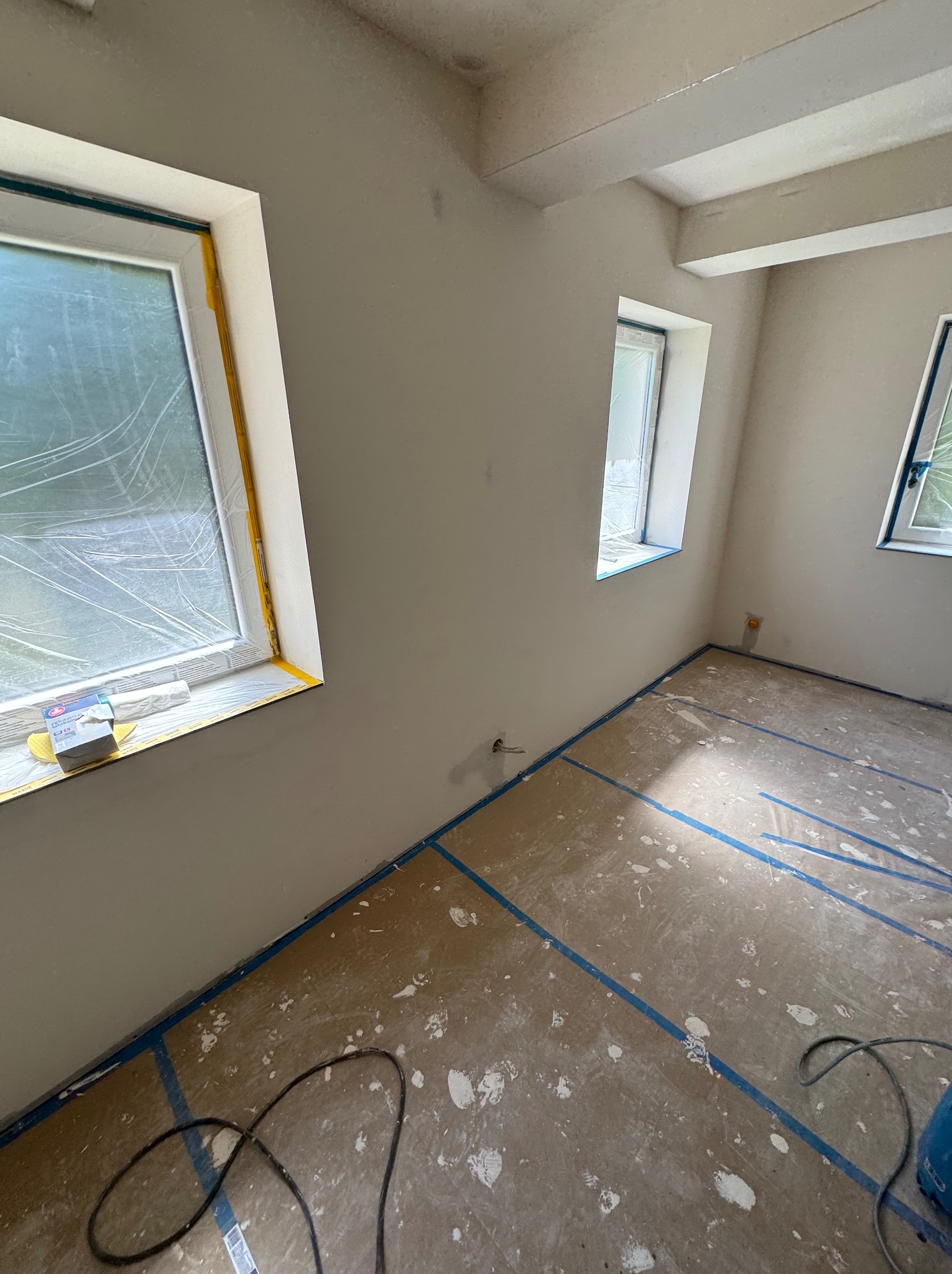 Pokój po nałożeniu gładzi, zabezpieczone okna folią i taśmą, podłoga zabezpieczona folią i taśmą malarską, widoczne ślady po gładzi.