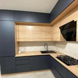 ArtVik - Nowoczesna kuchnia w odcieniach granatu i drewna, z czarną armaturą i płytą gazową, oświetlona naturalnym światłem.