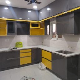 ArtVik - Nowoczesna kuchnia z szarymi szafkami i żółtymi akcentami, widoczny narożnik blatu, zlewozmywak ze stali nierdzewnej i torba na blacie.