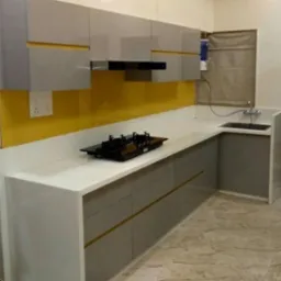 Nowoczesna kuchnia z szarymi szafkami z poziomymi złotymi akcentami, białym blatem, żółtą ścianą i czarną płytą grzewczą.