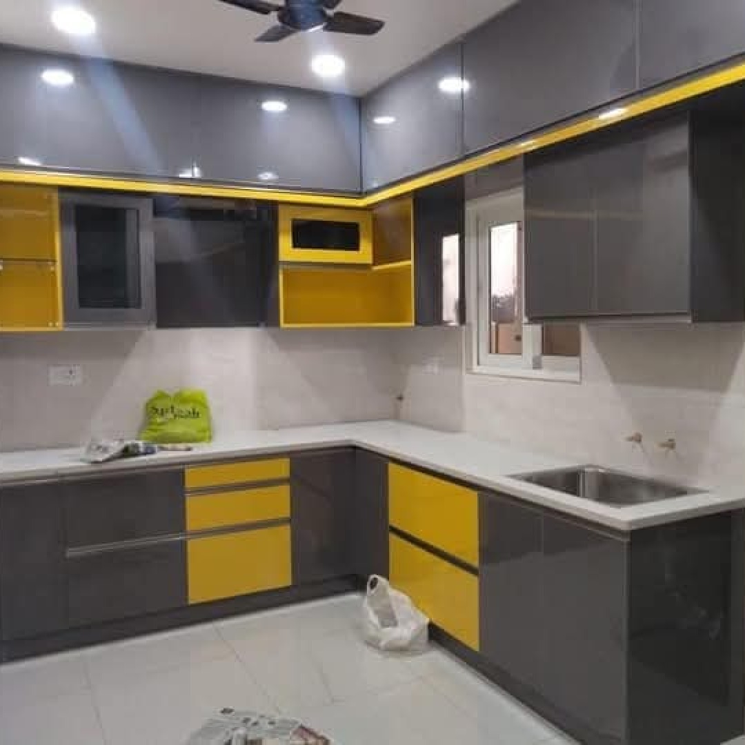 Nowoczesna kuchnia z szarymi szafkami i żółtymi akcentami, widoczny narożnik blatu, zlewozmywak ze stali nierdzewnej i torba na blacie.