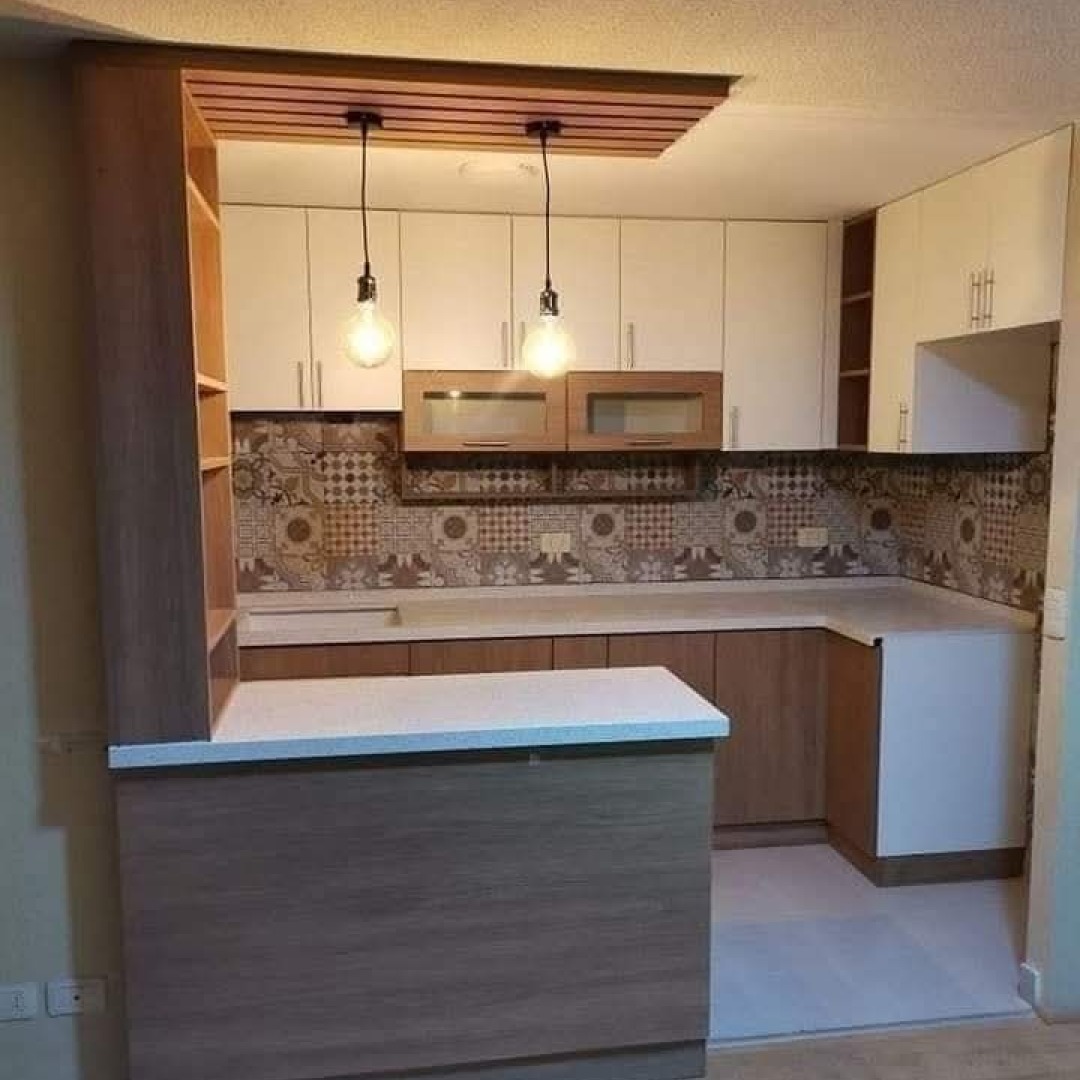 Jasna kuchnia z drewnianymi akcentami, wzorzystą mozaiką nad blatem i barem z białym blatem, oświetlona wiszącymi lampami z żarówkami Edisona.