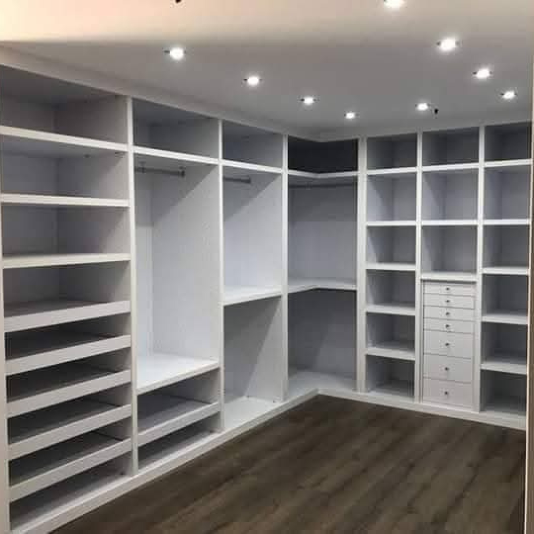 Przestronna, biała garderoba z licznymi półkami, szufladami i drążkami na ubrania, oświetlona punktowymi lampami sufitowymi, z ciemną podłogą imitującą drewno.