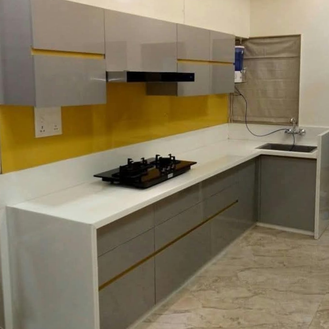 Nowoczesna kuchnia z szarymi szafkami z poziomymi złotymi akcentami, białym blatem, żółtą ścianą i czarną płytą grzewczą.