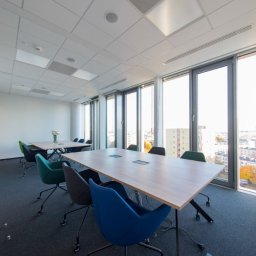 e-Support Sp. z o.o. - Jasne, nowoczesne biuro z dużymi oknami, widokiem na miasto, stołami konferencyjnymi z wbudowanymi gniazdami i ergonomicznymi krzesłami na kółkach.